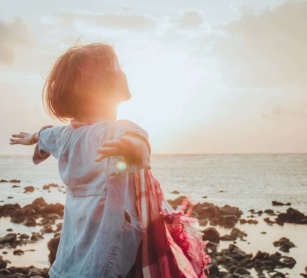 A carefree woman standing on a beach at sunset with arms outstretched as if flying.