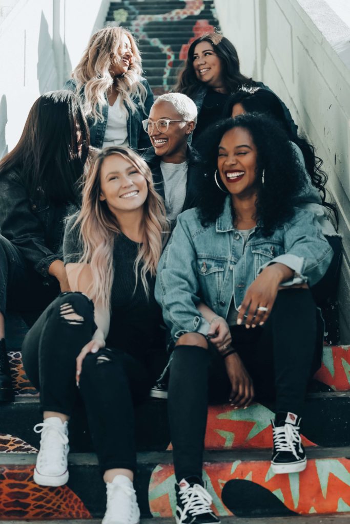 A group of six laughing college-age women sitting in a stairwell.