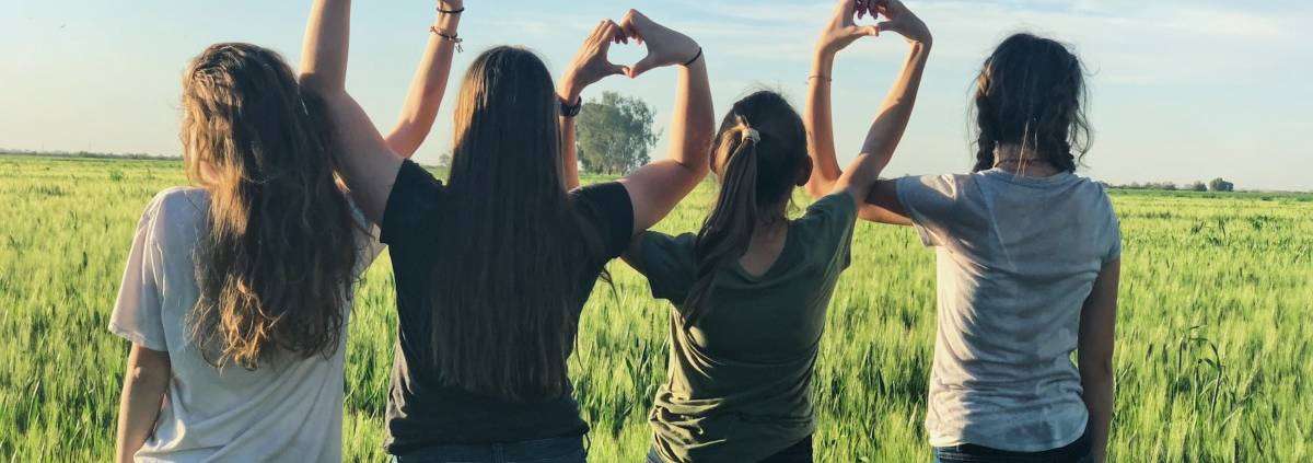 Group of girls in a field making hearts with their hands.