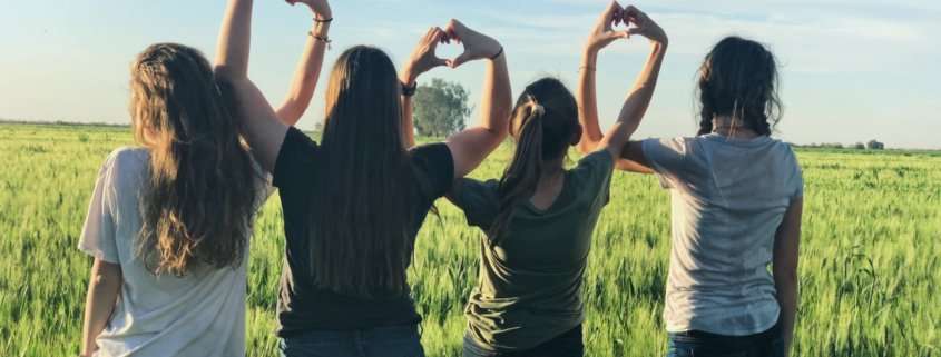 Group of girls in a field making hearts with their hands.