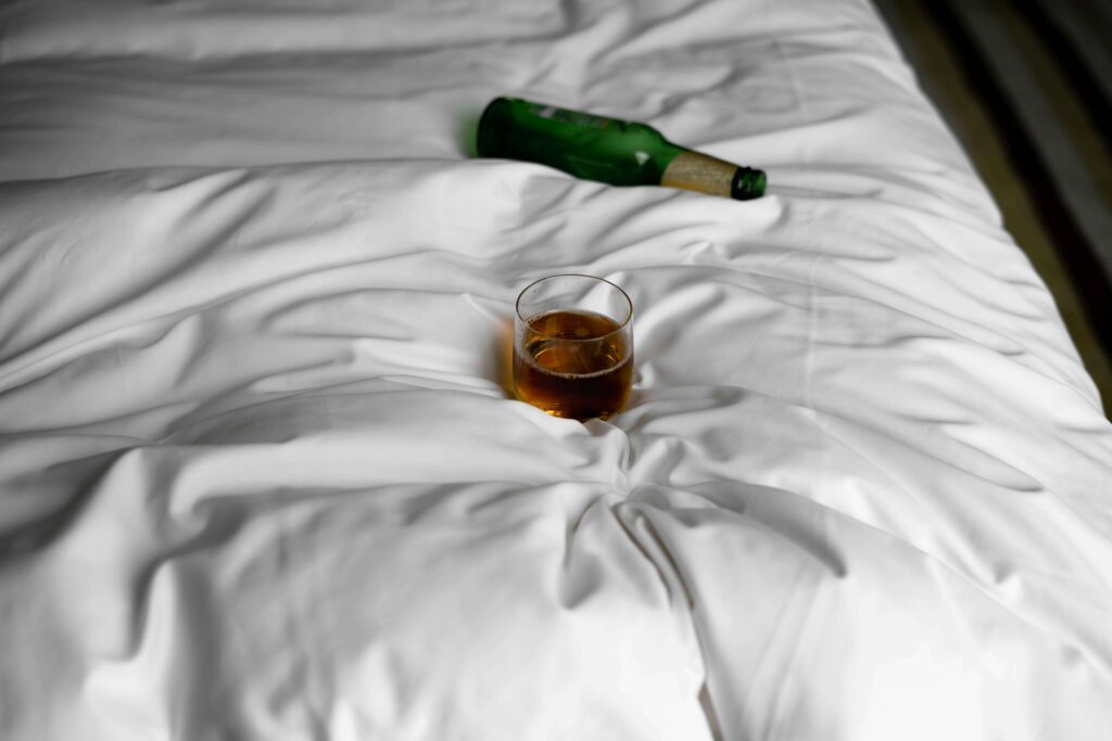 A bottle and glass of alcohol in a bed.