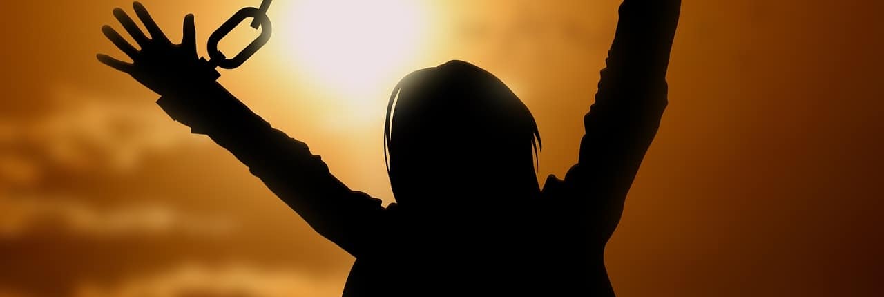 A silhouette of a person breaking out of the chains of adversity with the sunset in the background.