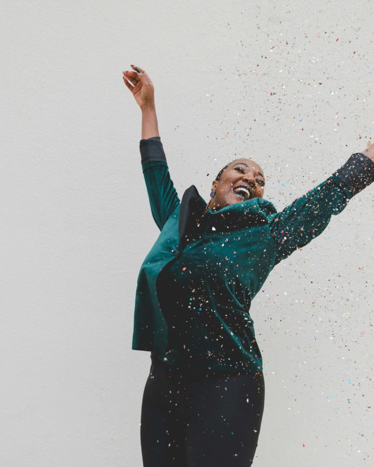 Woman jumping with joy and throwing confetti in celebration of reinventing herself.