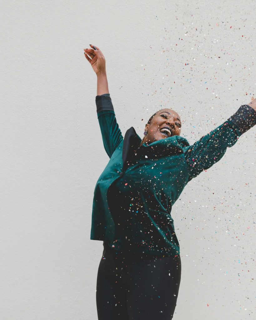 Woman jumping with joy and throwing confetti in celebration of reinventing herself.