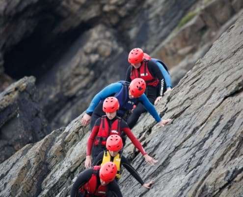 Five people wearing climbing gear show trust as they follow their guide along a steep rock cliff.