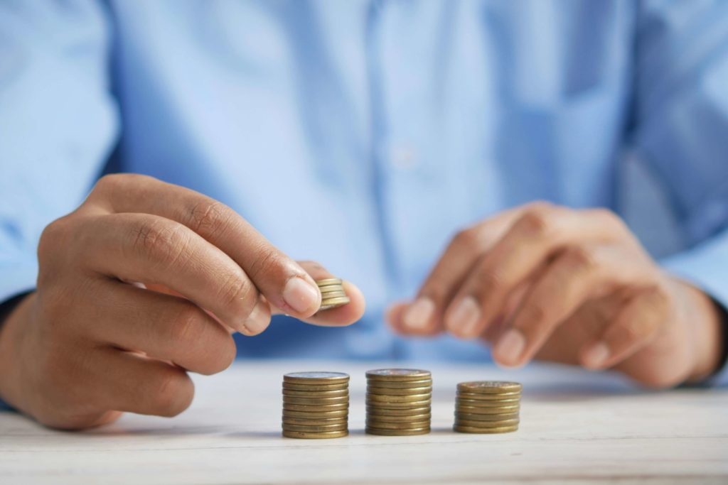 A man in a blue shirt is shown stacking coins in equal piles. Budgeting is the number one reason for conflict in couples.