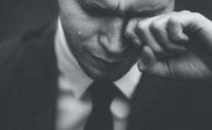 A man in a nice suit wiping tears from his eye.