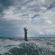 A hand is raised from turbulent water as a person drowns in stressful waters.