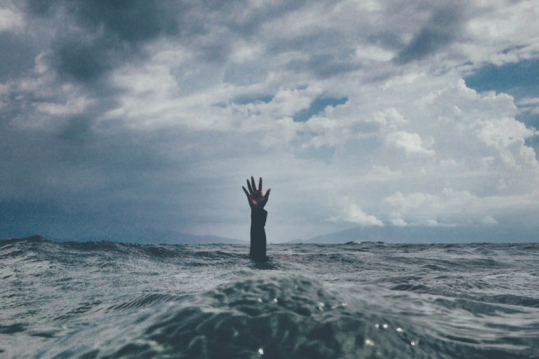 A hand is raised from turbulent water as a person drowns in stressful waters.