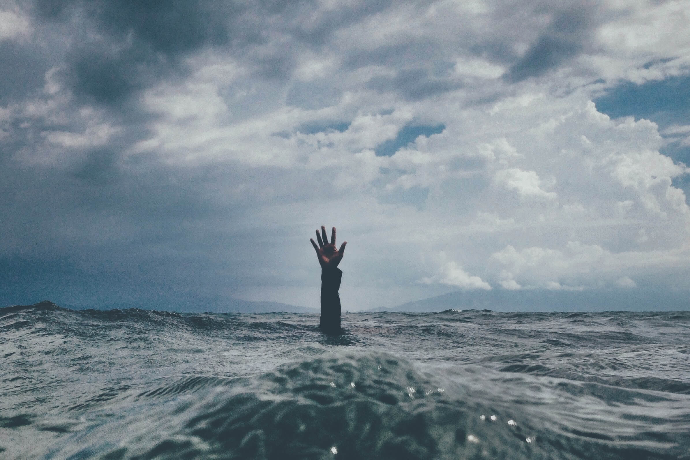 A hand is raised from turbulent water as a person drowns in stressful waters.