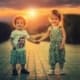 Two young toddler friends holding hands and walking at sunset holding hands.