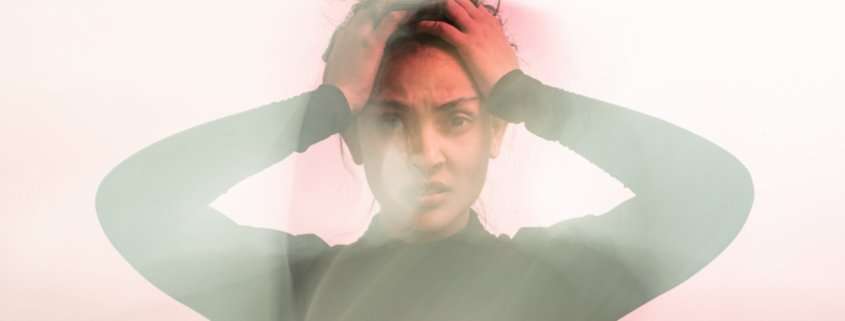 A woman in a black turtleneck is holding her head while overwhelmed against a pink background swirrling around her.