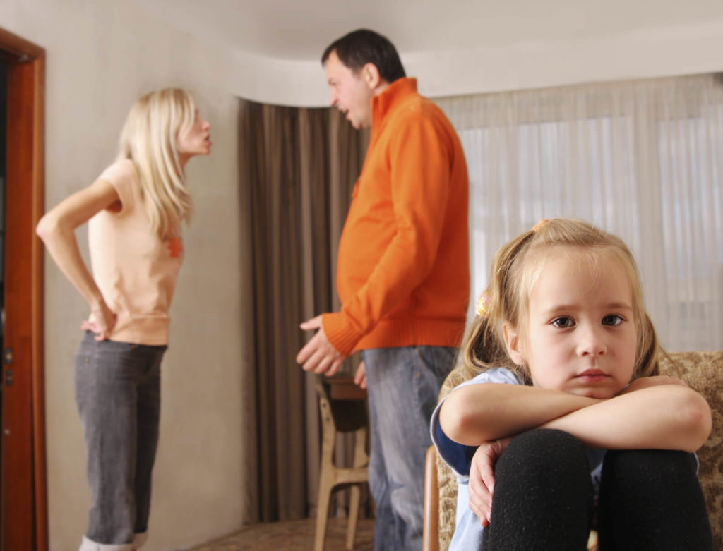 Divorced parents arguing in front of an upset child.