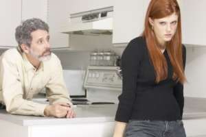 Father leaning on kitchen counter talking to teen girl who has her back turned to him.