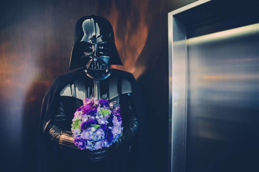 Darth Vader holding a colorful bouquet of flowers near an elevator.
